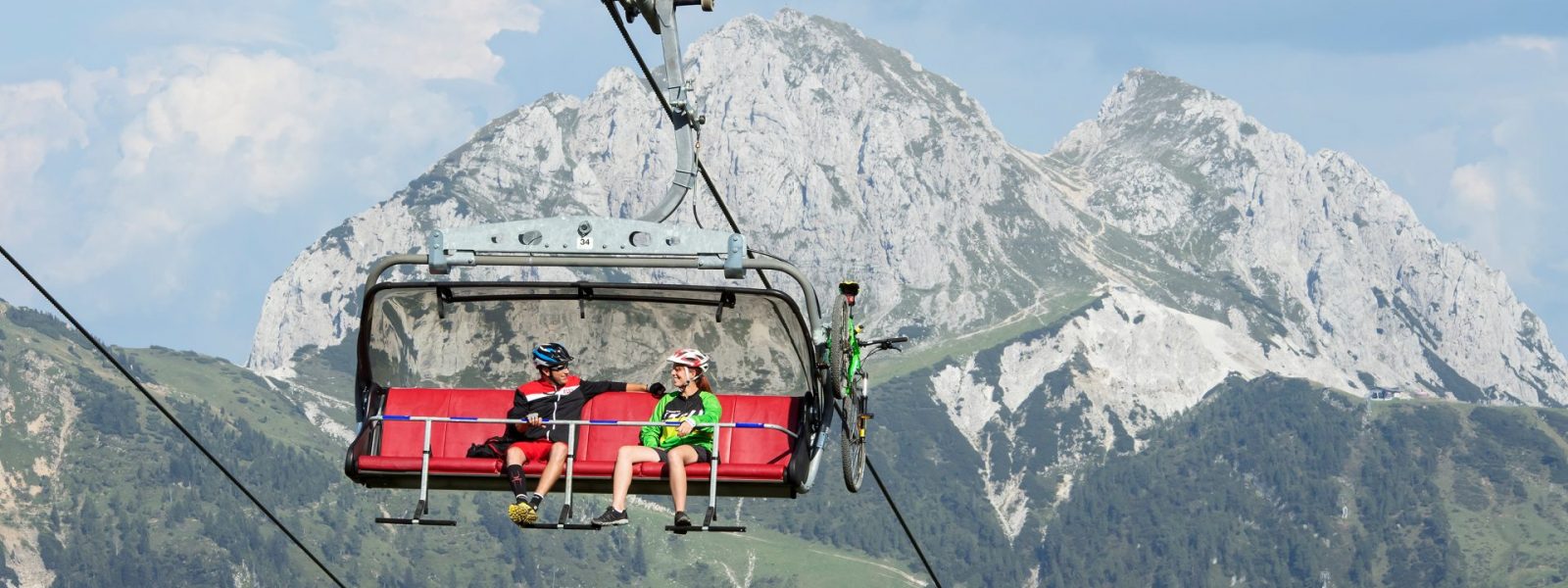 Mountainbiker die mit der Madritschenbahn am Nassfeld bergwärts fahren. Im Hintergrund der Gipfel des Gartnerkofel