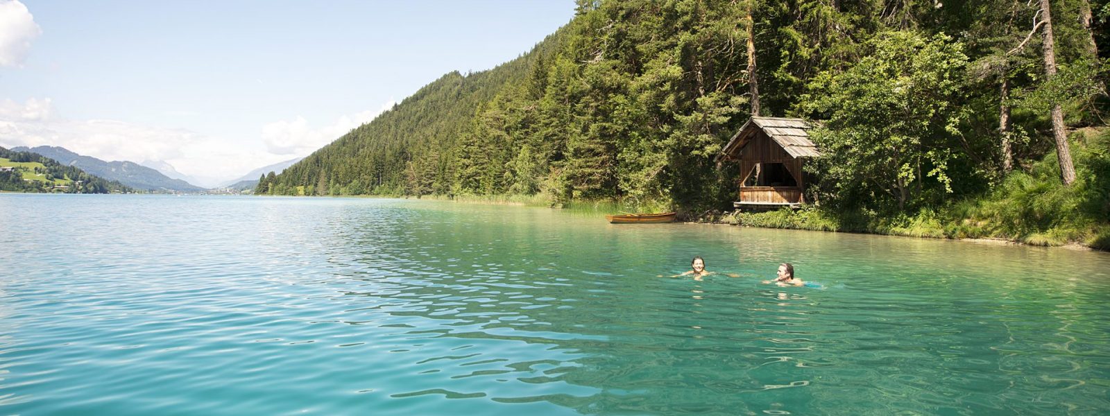 Zwei Schwimmer im türkisfarbenen Weissensee mit Wald im Hintergrund